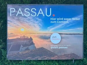 Plakatwerbung der Stadt Passau mit dem Slogan "Hier wird sogar Nebel zum Content" vor Nebelstimmung über der Stadt